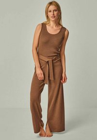 Braunes geripptes Strick-Top und weite Hose mit gebundenem Taillen-Detail, die seitliche Schlitze für Bewegungsfreiheit bietet.