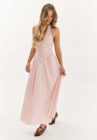 Ružová maxi šaty s halter výstrihom, obtiahnutým korzetom, splývavou sukňou a bočnými vreckami. Skombinované s plochými topánkami s obrazcom zvierat. Hladký bavlnený materiál.