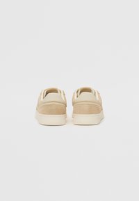 Sneaker beige con tomaia in pelle liscia e dettagli in suede. Forma arrotondata, linguette sul tallone in contrasto e design minimalista. Suola piatta di colore chiaro.