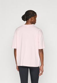 Ροζ ανοιχτόχρωμη, φαρδιά μπλούζα με στρογγυλή λαιμόκοψη και κοντά μανίκια, κατασκευασμένη από μαλακό βαμβακερό ύφασμα. Διαθέτει ίσια γραμμή και μινιμαλιστικό σχέδιο.