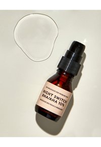 Braune Glas-Tropfflasche mit einem schwarzen Drehverschluss. Das Etikett trägt die Aufschrift "NIGHT SWITCH BHA/AHA 10%." Eine klare Flüssigkeit liegt auf einer hellen Oberfläche.