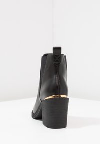 Černá kožená kotníková bota s masivním podpatkem, elastickými bočními panely a zlatým akcentem na podpatku. Texturovaná gumová podrážka.