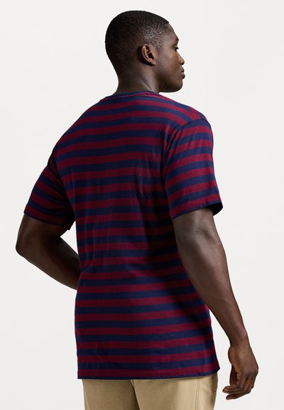 Μπλουζίτσα με κοντά μανίκια σε ναυτικό και μπορντώ ρίγες, χαλαρή εφαρ�μογή, στρογγυλή λαιμόκοψη και μαλακή υφή. Ορατές λεπτομέρειες ραφής στο πίσω μέρος.