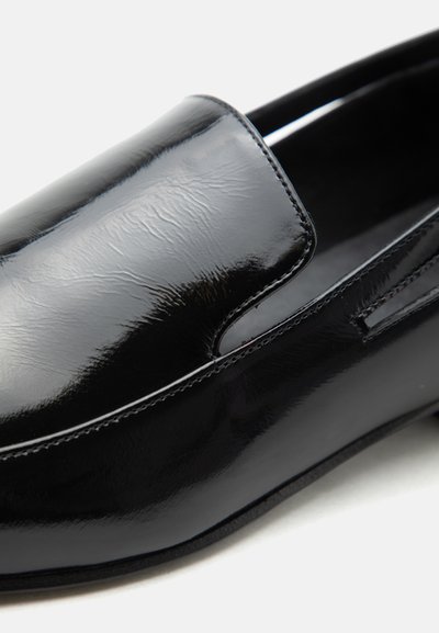 Μαύρο γυαλιστερό δερμάτινο μοκασίνι με λεία στρογγυλεμένη μύτη και διακριτικές ραφές στα πλάγια.