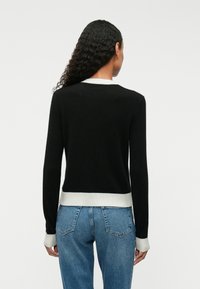 Un pull noir à manches longues, avec un ourlet et des poignets en maille côtelée gris clair. Le dos est uni avec une texture lisse, porté avec un jean bleu.