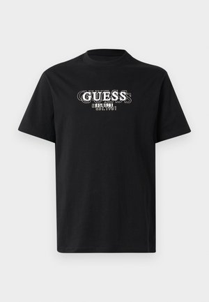 Camiseta de algodón negra con un estampado gráfico blanco del nombre de la marca "GUESS" y el año de establecimiento "EST. 1981" en la parte frontal.