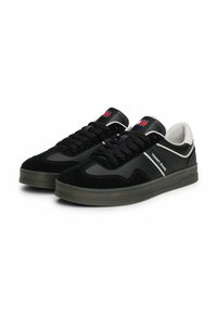 Czarne sneakersy wykonane z zamszu i skóry, z białym akcentem na pasku, czarnym sznurówkami i logo na języku. Gruba gumowa podeszwa.