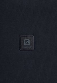 Marineblauem Stoff mit texturierter Oberfläche; ausgestattet mit einem quadratischen schwarzen Patch mit dem eingeprägten Text "GABBANO" und einem Logodesign.