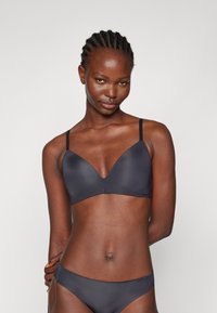 Reggiseno wireless grigio scuro con una superficie liscia e opaca, dotato di scollatura profonda e spalline sottili e regolabili. Design semplice senza decorazioni.