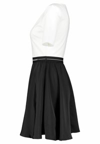 Vit kortärmad topp kombinerad med en svart utsvängd kjol, med en slät textur och ett kontrasterande midjeband med textdetaljer.