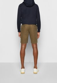 Braune Shorts aus Baumwolle mit einem klassischen Schnitt, zwei Gesäßtaschen und glatter Textur, kombiniert mit einem navyblauen Kapuzenpullover.