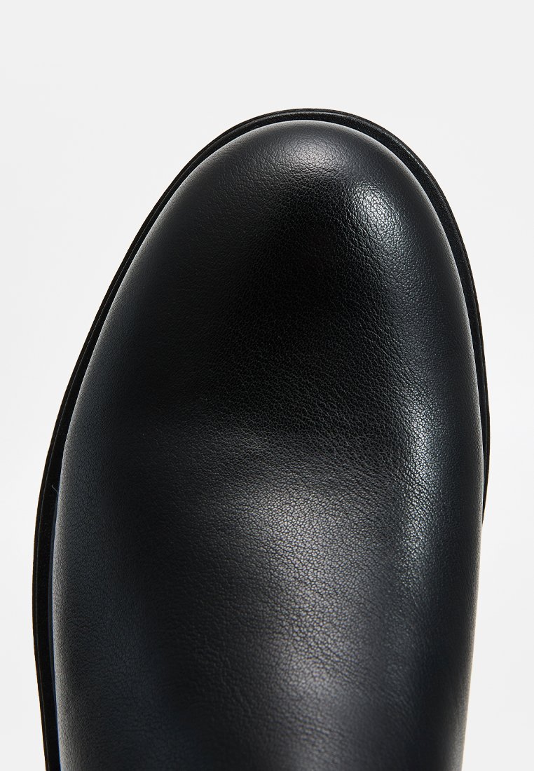 Bottine noire en cuir avec un bout rond, texture lisse et minimalisme dans les détails. Elle est dotée d'une semelle noire unie et d'une finition polie.