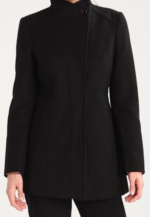 Manteau noir cintré pour femme avec un col haut et un seul bouton visible près de l'encolure, manches longues et une silhouette épurée.