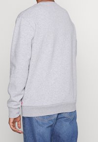 Felpa grigia con maniche lunghe, tessuto textured, polsini e orlo a coste, branding minimale sul lato inferiore, vestibilità rilassata, collo alla marinara classico.