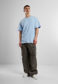 T-shirt oversize bleu clair avec un col rond, associé à un pantalon cargo gris foncé avec des poches latérales et des baskets blanches.