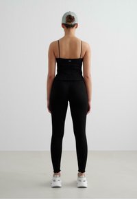 Svart ribbad linne med justerbara spaghetti-burkar och scalloped nederkant, matchat med åtsittande svarta leggings och vita sneakers.