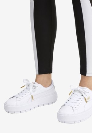 Witte platform sneakers met een textuur bovenkant, vetersluiting aan de voorkant, gouden accenten en contrasterende stiksels. Gemaakt met zwart-witte leggings.