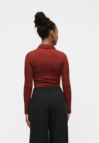 Μακρυμάνικη πορτοκαλί μπλούζα πόλο με γιακά, σε συνδυασμό με μαύρο παντελόνι φαρδύ στο πόδι. Λείο ύφασμα, εφαρμοστή σχεδίαση και μήκος μέχρι τον αστράγαλο.