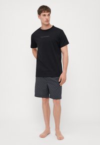 Fekete, rövid ujjú póló, visszafogott Calvin Klein logóval, sötét mintás rövidnadrággal párosítva. Egyszerű dizájn, puha anyag, látható varratok nélkül.