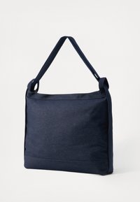 Sac à épaule en toile bleu marine avec une finition texturée, une seule sangle réglable et une forme carrée. Présente des coutures visibles le long des coutures.