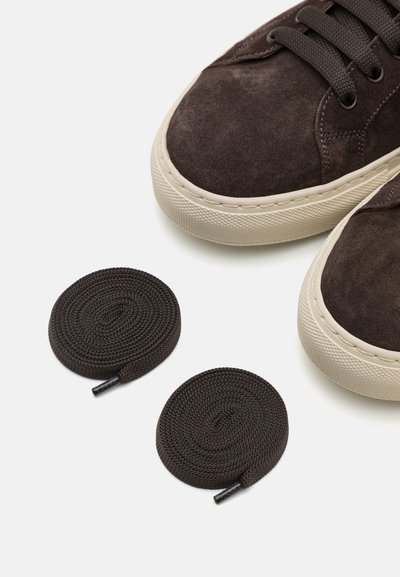 Baskets en suède marron avec semelles en caoutchouc crème, dotées de lacets ronds de couleur marron assortie, placées à côté de deux lacets spiralés de la même couleur.