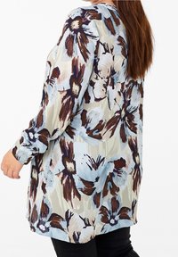 Bloemencam blouse met lange mouwen in een lichtblauwe, crème en bruine patroon. Lichtgewicht stof met een losse pasvorm, met knoopdetails op de manchetten.