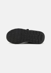 Semelle de chaussure de sport noire en caoutchouc avec une texture adhérente, ornée du logo Adidas, conçue avec un profil de bande de roulement pour une meilleure traction.