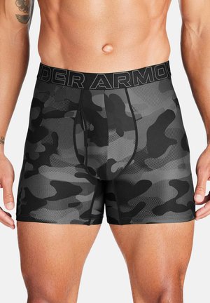 Torso maschile indossando boxer Under Armour mimetici neri e grigi con fascia in vita con logo e tatuaggio visibile sul braccio sinistro.