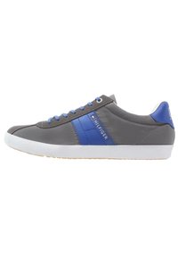 Chaussure de sport grise avec des accents bleus, dotée d'une tige en cuir lisse, d'une semelle en caoutchouc blanche et de lacets bleus. Marque visible sur le côté.