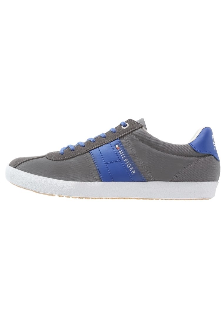 Chaussure de sport grise avec des accents bleus, dotée d'une tige en cuir lisse, d'une semelle en caoutchouc blanche et de lacets bleus. Marque visible sur le côté.