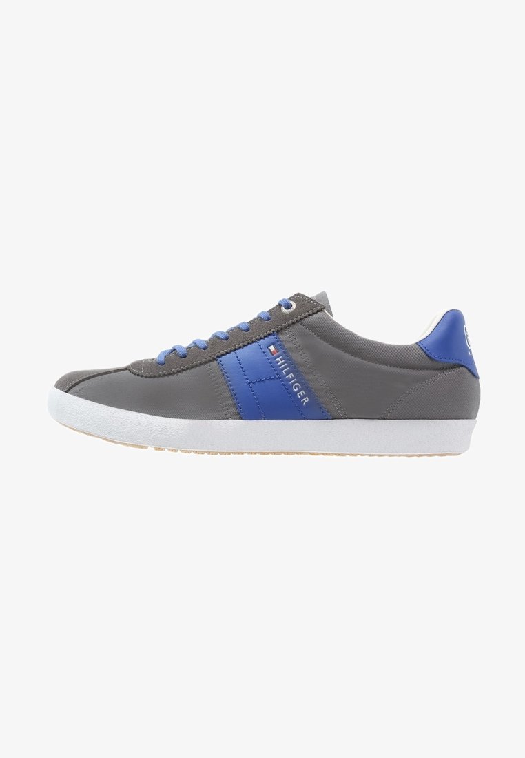 Chaussure de sport grise avec des accents bleus, dotée d'une tige en cuir lisse, d'une semelle en caoutchouc blanche et de lacets bleus. Marque visible sur le côté.