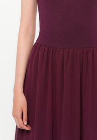 Burgundy dress with a fitted bodice and flowing, gathered chiffon skirt. Smooth texture on top contrasts with the soft, airy fabric below.
