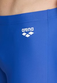 Bañador azul hecho de un material suave y ligero. Presenta un logo blanco de "arena" y tres formas de diamante. Acabado sin costuras en la cintura.