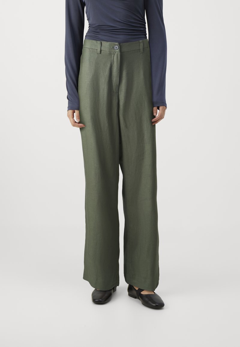 Pantalon large en lin vert avec fermeture à boutons sur le devant, associé à un haut manches longues bleu marine. Le tissu présente une texture lisse et douce.