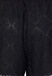 Tela de encaje negro con un intrincado patrón floral que presenta texturas variadas y detalles de calado, cayendo suavemente en un diseño en capas.