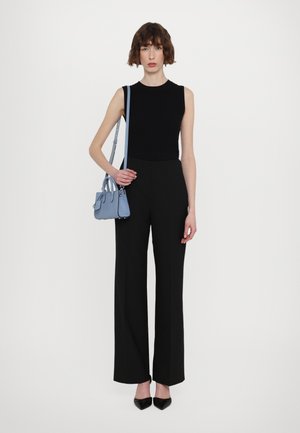 Black sleeveless top paired with high-waisted black trousers. Holding a small light blue handbag, wearing black pointed shoes.