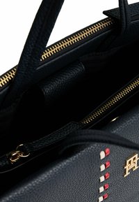 Borsa a tracolla in pelle nera con texture, hardware dorato, chiusura a zip e accenti decorativi di colore rosso e bianco su un lato.