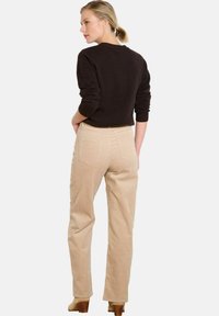 Šviesiai rudos kordūrinių kelnių tiesaus kirpimo, su užpakalinėmis kišenėmis ir subtilia tekstūra, derinamos su juoda megztine.