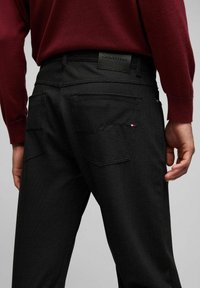 Pantalons à carreaux noirs avec un tissu texturé. Présente une étiquette en cuir noir à la taille et deux poches arrière.