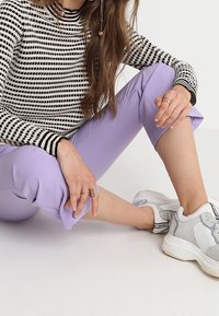 Zwart-wit gestreepte lange mouwen top gecombineerd met lavendel geknipte broek en lichtgrijze sneakers, die een casual, ontspannen stijl benadrukken.