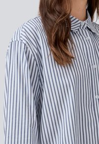 Button-up skjorte med lyseblå og marineblå lodrette striber, lavet af bomuld. Har en klassisk krave og knaplukning. Blød tekstur.