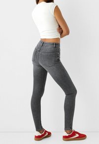 Jeans ajustados grises con bolsillos delanteros y traseros, combinados con zapatillas rojas con detalles blancos y marrones; estilo ceñido y textura suave.