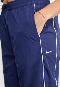 Jūras spēku sporta bikses, kas izgatavotas no viegla materiāla ar baltām sānu svītrām un mazu Nike logotipu. Iezīmē elastīgu jostasvietu un kabatas.