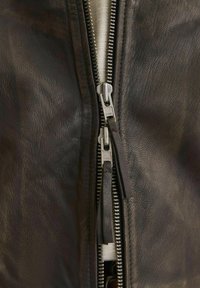 Close-up of a double silver zipper on a dark brown leather jacket partially unzipped to show white fabric underneath.