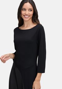 Zwarte jurk met een ronde halslijn en lange mouwen, met een aansluitend bovenlijfje en een vloeiende onderrok met een subtiele asymmetrische vorm.