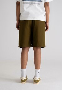 Mørke olivengrønne shorts laget av lett stoff, med rett snitt, som ender rett over kneet. Kombinert med hvite Nike-sneakers.