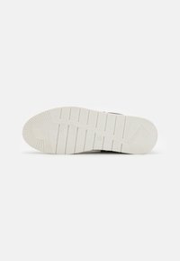 Semelle d'une chaussure en caoutchouc blanche avec motifs texturés pour l'adhérence, rainures et nom de la marque embossé près du talon sur un fond uni.