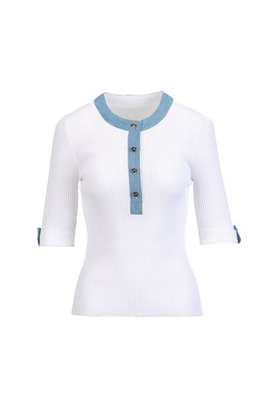 Chemise blanche côtelée avec un col bleu clair et une patte de boutonnage, dotée de manches trois-quarts et de poignets retroussés. Les boutons sont en métal.