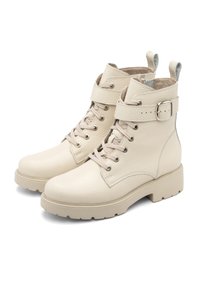 Botas de tobillo de cuero beige con acabado texturizado, que presentan un cierre de cordones en la parte delantera, correa ajustable, detalle de hebilla y suela de goma gruesa.