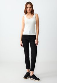 Canotta bianca a costine abbinata a pantaloni neri slim-fit e sneakers nere, su uno sfondo minimale chiaro.